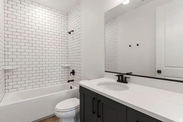 Built-in bathtub with subway tile surround, matte black shower fixtures, vanity with dark cabinetry, white countertop, and integrated sink