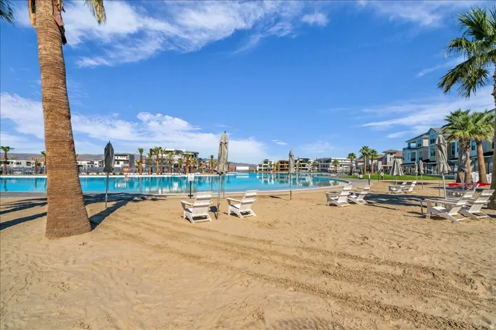 Sand beach area with palm trees, a large blue water lagoon, and residential structures in the background