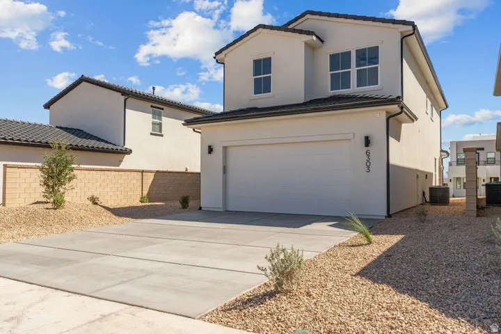 Stucco exterior with a two-car garage, dark tile roof, and a concrete driveway