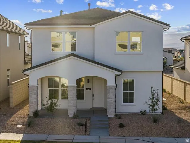 Two-story stucco exterior with a covered entry, dark tile roof, and stone-clad porch columns