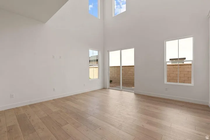 Vaulted ceiling, wood-finish flooring, white walls, multiple windows, and a sliding glass door