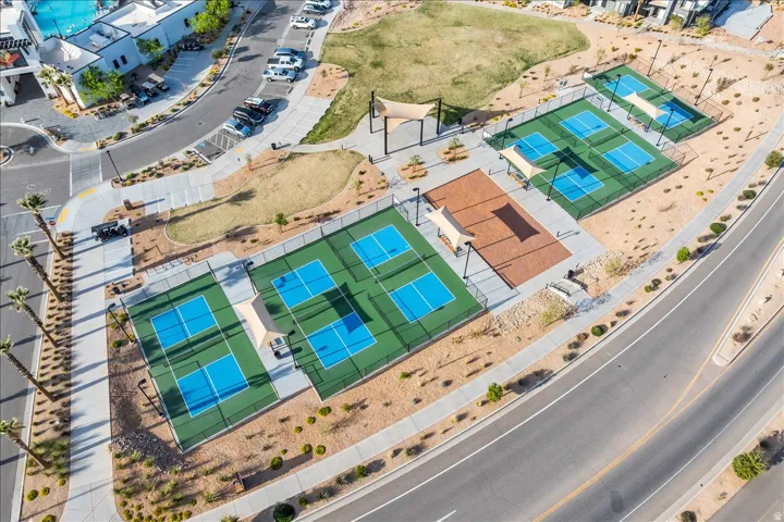 Multiple pickleball courts with perimeter fencing, shaded seating areas, extensive paved pathways, and manicured desert landscaping