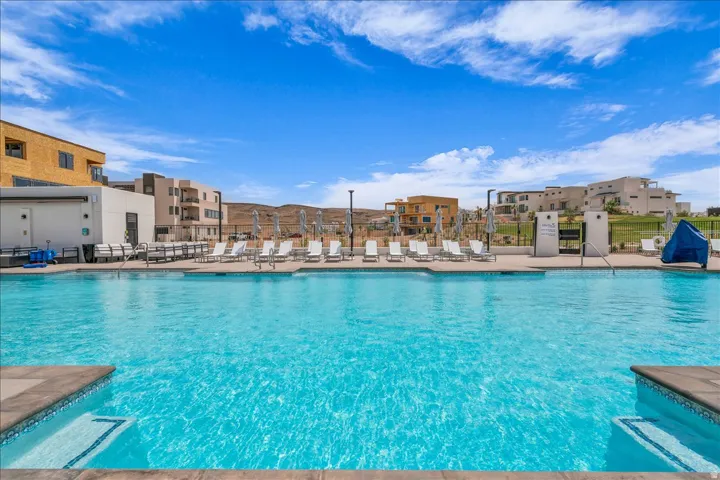 Expansive swimming pool with integrated steps, surrounded by a paved deck with lounge seating and shade structures, and an array of modern residential architecture