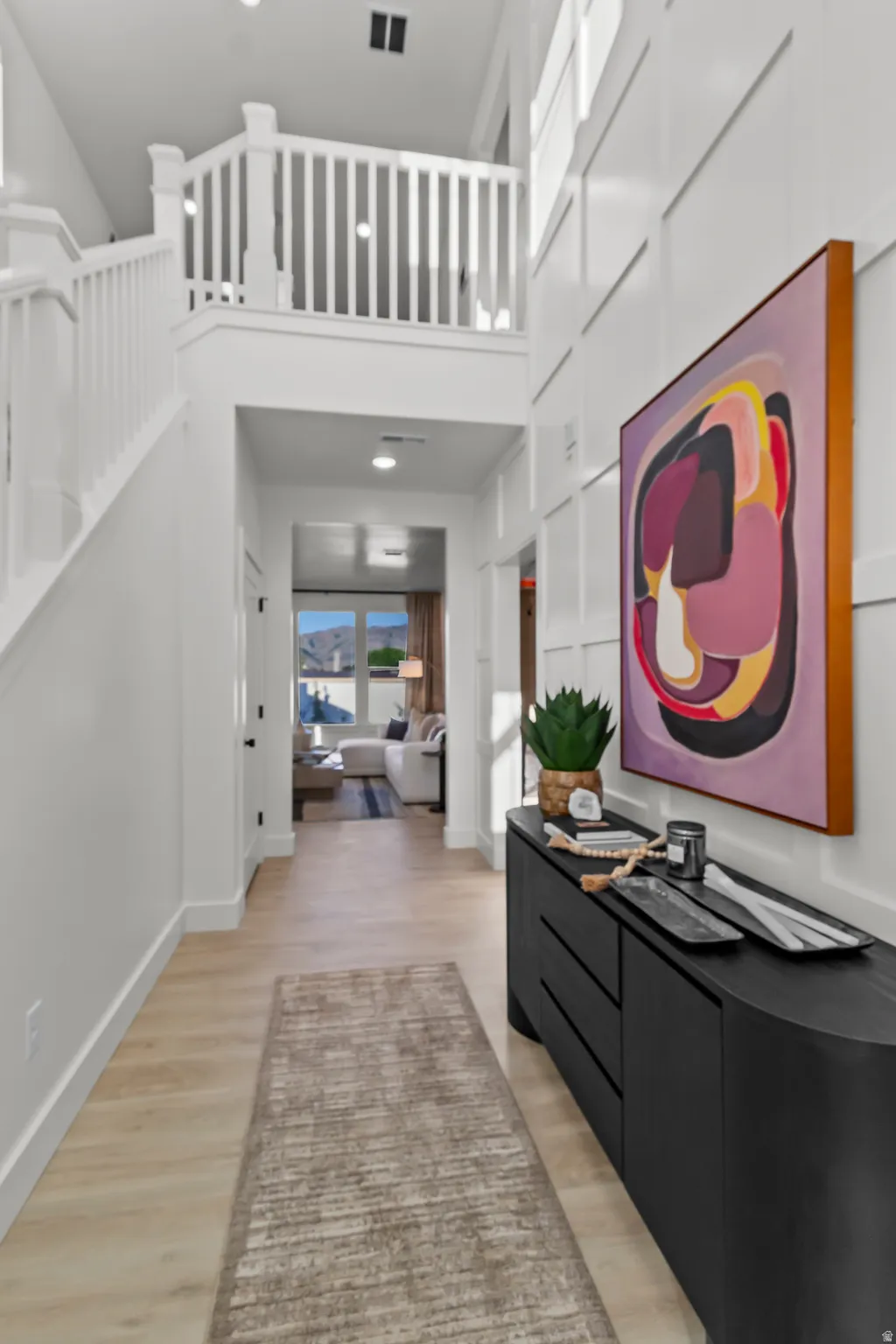 Two-story entry with wood-finish flooring, white paneling, and a white staircase with balusters