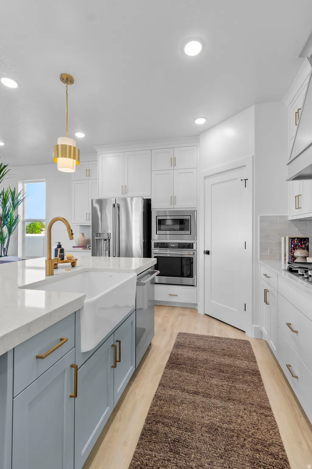 Kitchen featuring a white farmhouse sink, light blue island cabinetry, white perimeter cabinetry, stainless steel appliances, and wood-finish flooring