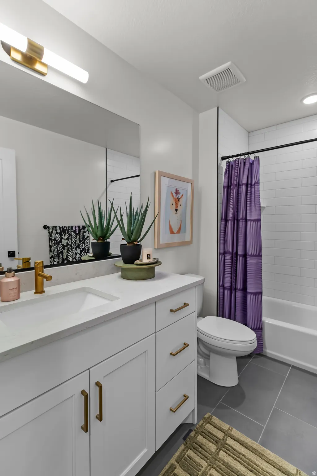 White shaker-style vanity with brass hardware, integrated rectangular sink, and light-toned countertop