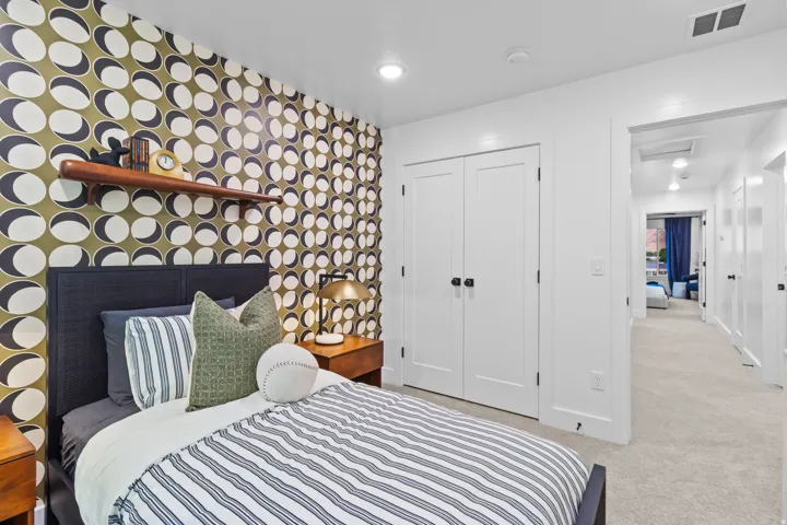 Accent wall with a graphic pattern, recessed ceiling lighting, built-in wooden shelf, dual closet doors with dark hardware, and carpet flooring