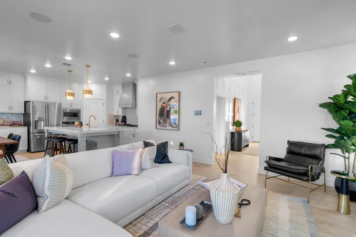 Open-concept living space with light-tone wood-finish flooring, recessed lighting, and a kitchen featuring white cabinetry and stainless steel appliances