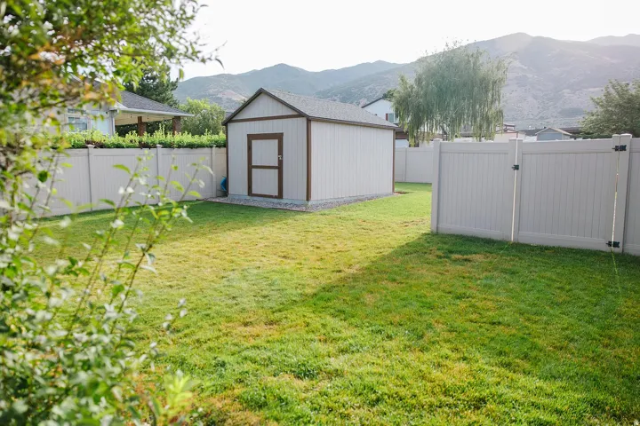 Expansive grassy yard with a white panel fence and a gate, featuring a shed with a brown-trimmed door and a brown roof