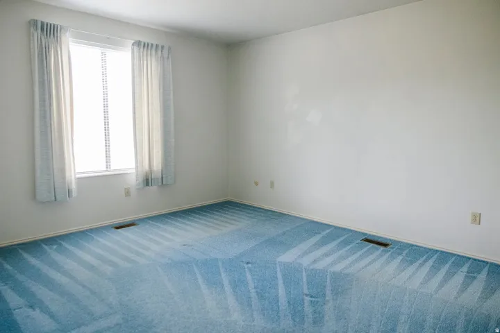 Bright interior room featuring a window with blinds, light blue carpeting, and white walls
