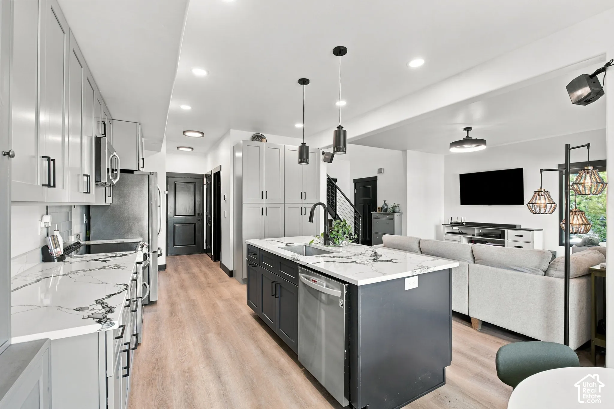Light wood-finish flooring, recessed lighting, kitchen island with sink, dark gray cabinetry, and light-toned countertops