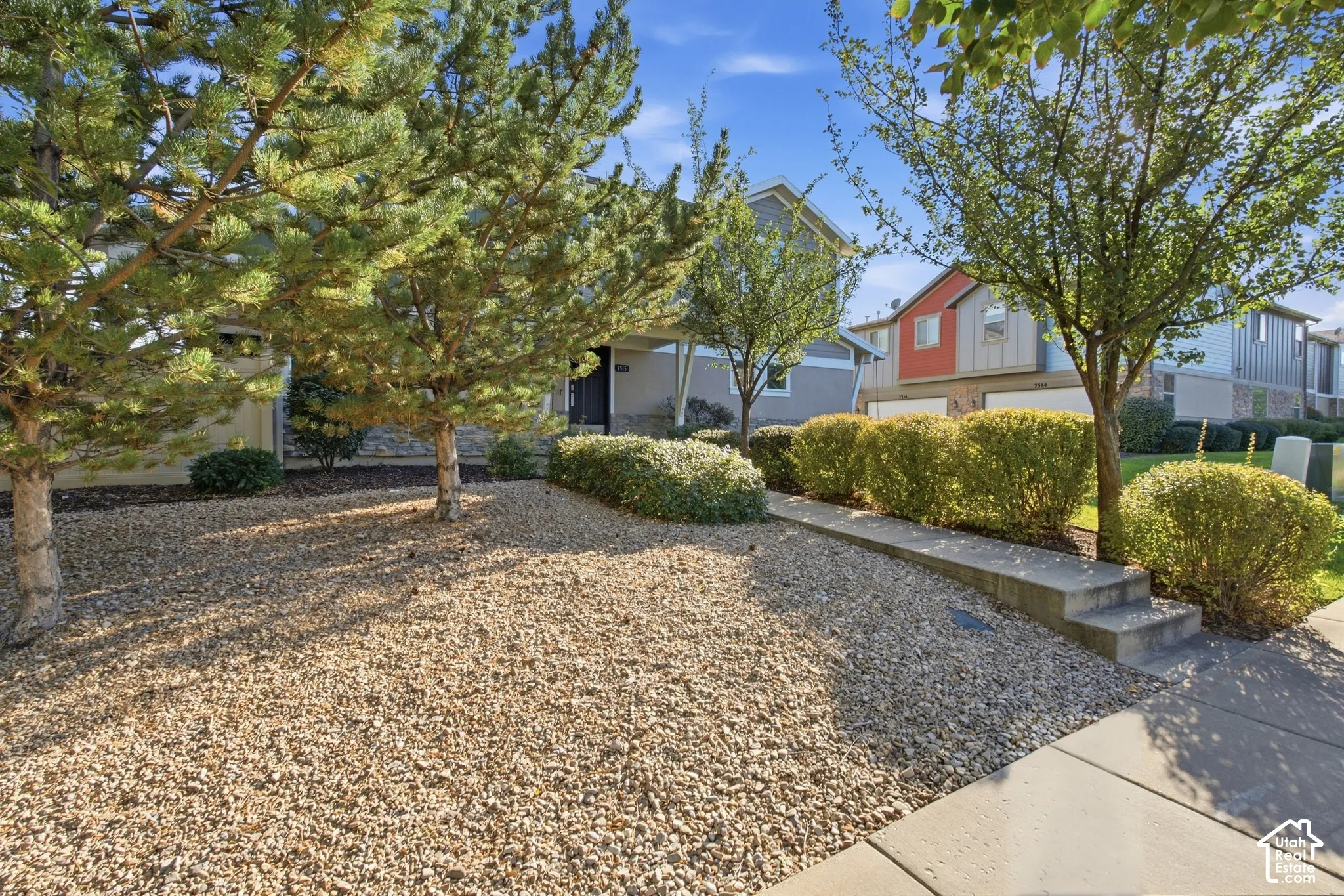 Landscaped front yard with gravel, mature trees, manicured hedges, and a concrete walkway