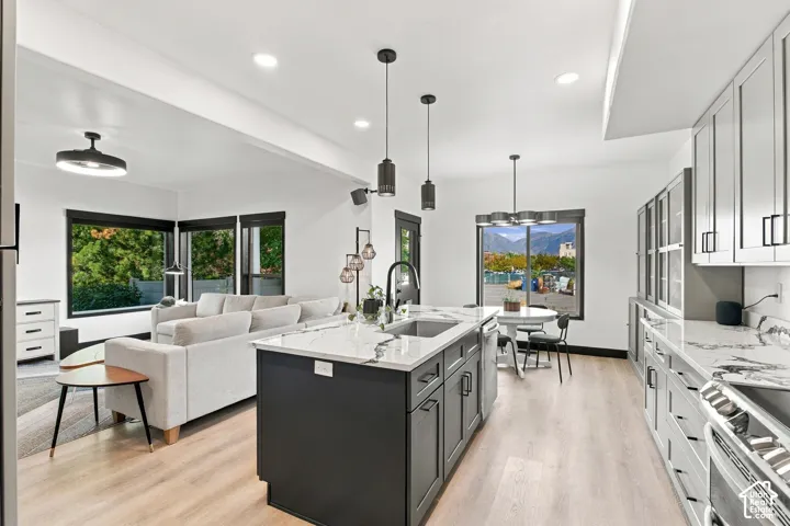 Open-concept kitchen and living area featuring wood-finish flooring, recessed lighting, a kitchen island with sink, and white countertops