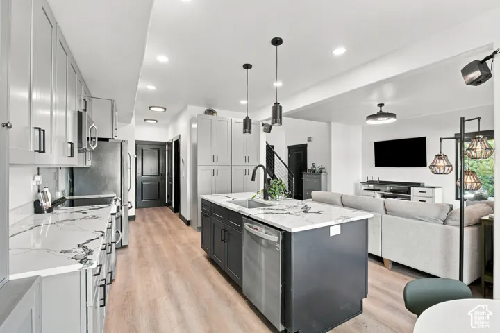 Light wood-finish flooring, recessed lighting, kitchen island with sink, dark gray cabinetry, and light-toned countertops