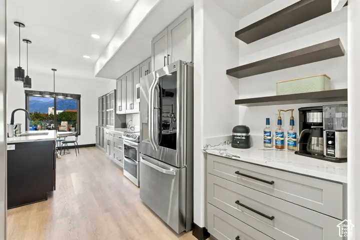 Modern kitchen featuring light wood-finish flooring, light grey cabinetry with dark hardware, stainless steel appliances, and an island with a black sink and faucet