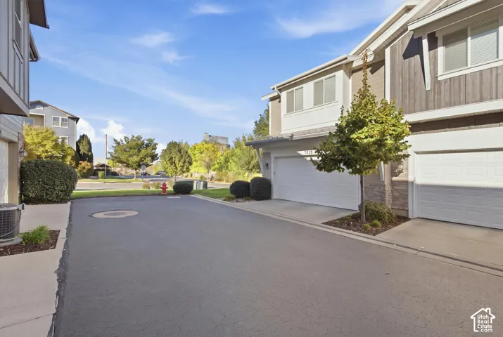 Two-car garage with white panel door, exterior wall with horizontal siding and stone accents, mature landscaping, paved driveway, and concrete walkway