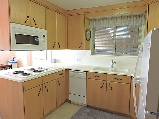 Kitchen featuring light wood-finish cabinetry, solid surface countertops, a white over-the-range microwave, and a white dishwasher