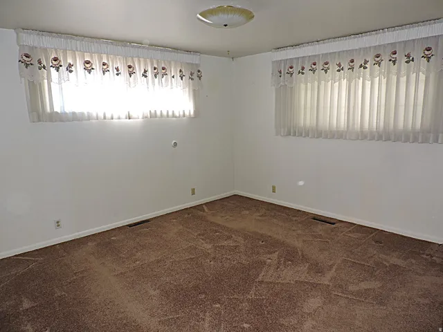 Wall-to-wall carpeting with white baseboards, two windows with blinds, and an overhead flush mount light fixture