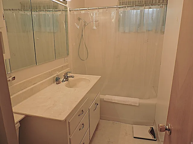Vanity with integrated sink, tri-fold mirrored medicine cabinet, wall-mounted light fixture, and a shower/tub combination