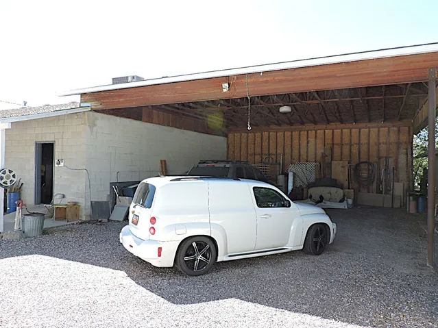 Gravel driveway leading to a spacious covered carport with exposed wood framing