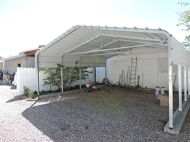 Gravel parking area featuring a metal carport structure and a white picket fence