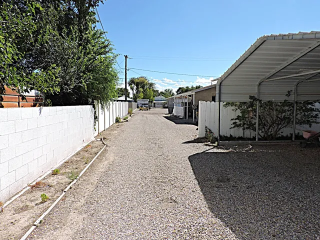 Gravel driveway with a white block wall, established trees, and a covered carport structure