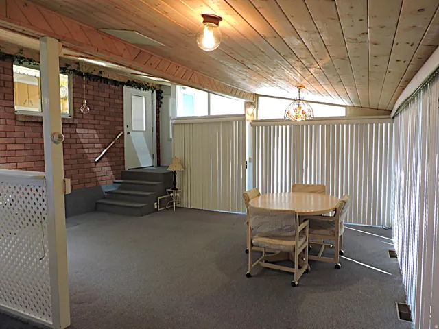 Carpeted sunroom with a wood-planked ceiling, brick wall, and vertical blinds