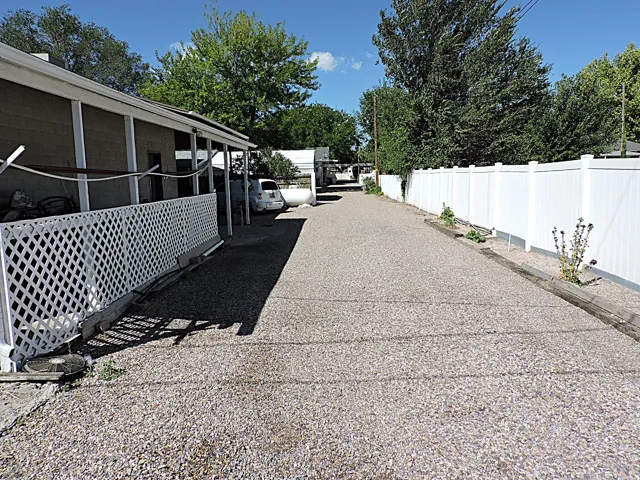 Gravel driveway with a white privacy fence and a covered side porch featuring white lattice