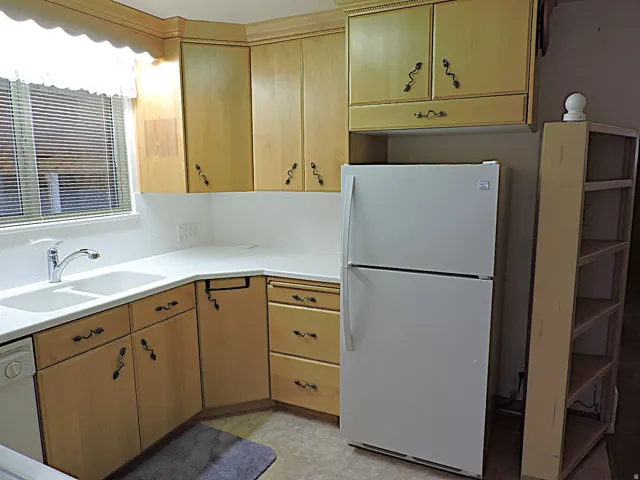Light wood-finish cabinetry with decorative hardware, white countertops, and a double basin sink