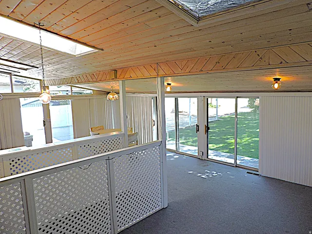 Sliding glass doors, wood-paneled ceiling, skylight, lattice railing, and ceiling-mounted light fixtures