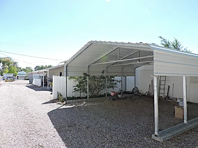 Covered carport with metal frame construction and gravel grounds, providing sheltered outdoor space