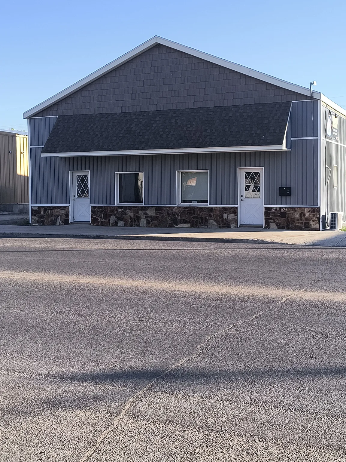 Gable roofline with shingle siding accent, horizontal siding, stone veneer foundation, and two entry doors with diamond-pane inserts