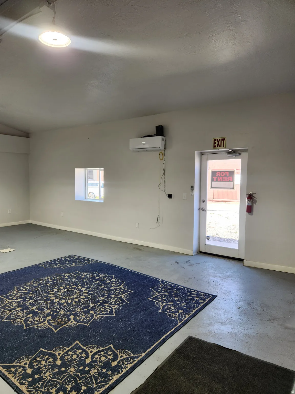 Recessed overhead lighting, mini-split air conditioning unit, glass-paneled entry door, and painted concrete flooring