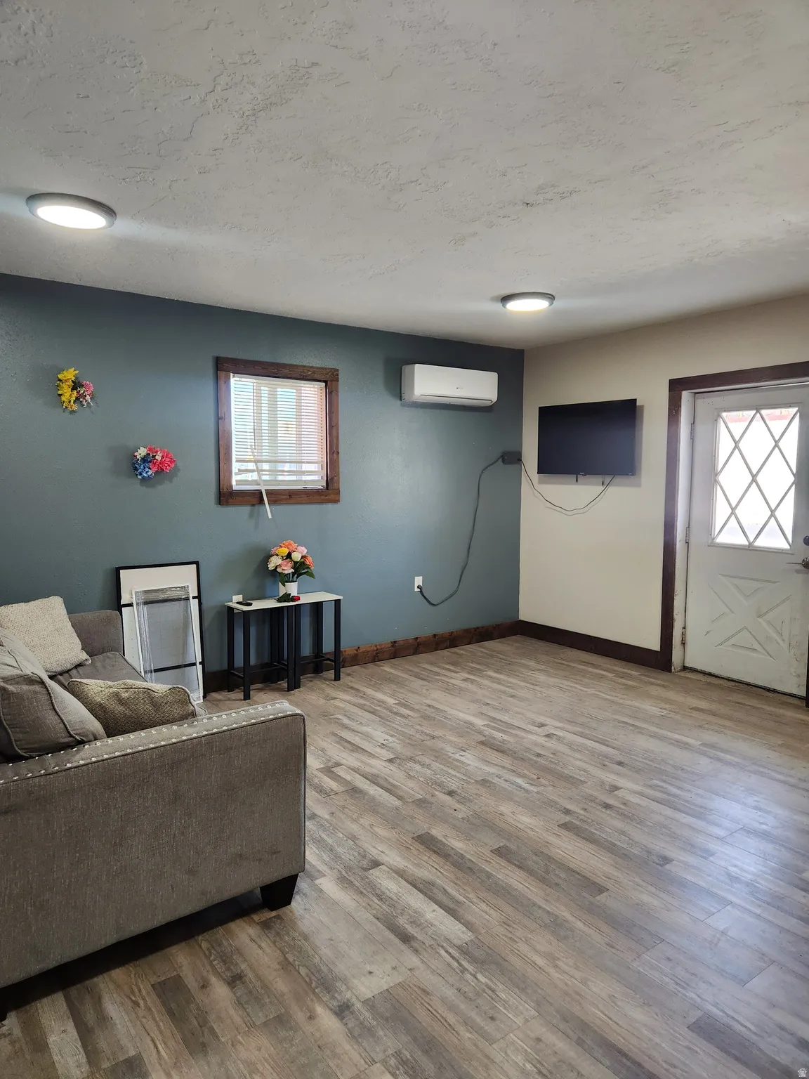 Wood-finish flooring, recessed lighting, wall-mounted air conditioning unit, and a diamond-patterned door