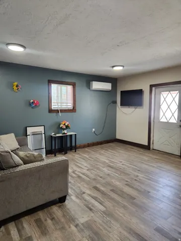 Wood-finish flooring, recessed lighting, wall-mounted air conditioning unit, and a diamond-patterned door