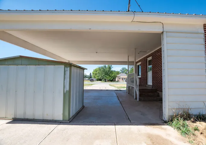 Covered carport with concrete flooring, brick exterior, and white siding