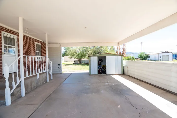 Covered carport with concrete flooring, direct entry to the brick-faced residence, and a metal storage shed