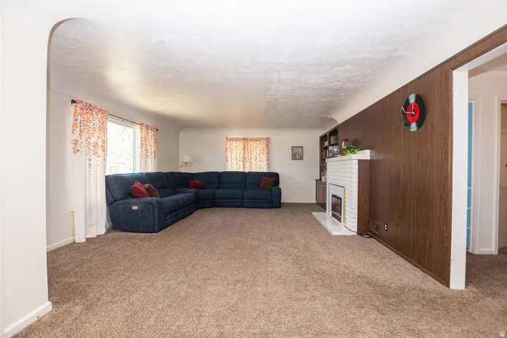 Living area with carpeted flooring, white walls, wood paneling, and a built-in fireplace with a white brick surround