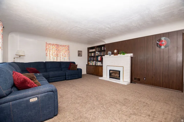 Carpeted living area featuring a white brick fireplace with a dark insert, wood-paneled wall, and built-in shelving