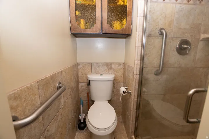 Wall-mounted grab bars, full tile wainscoting, glass-enclosed shower, and built-in overhead cabinetry