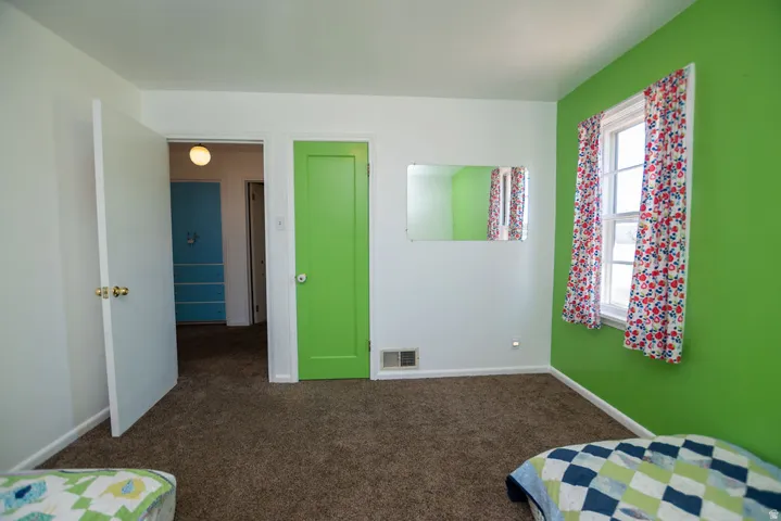 Brown carpet flooring, white walls, green accent wall, white window frame, and a green interior door