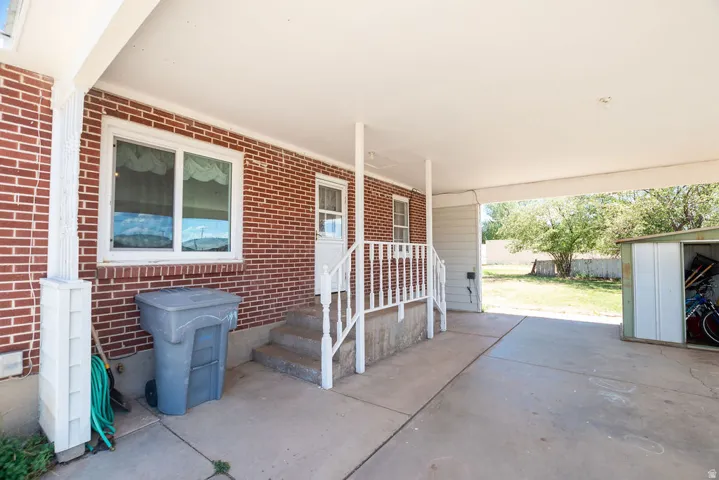 Covered patio area featuring a brick exterior wall, white framed windows, and a metal storage shed