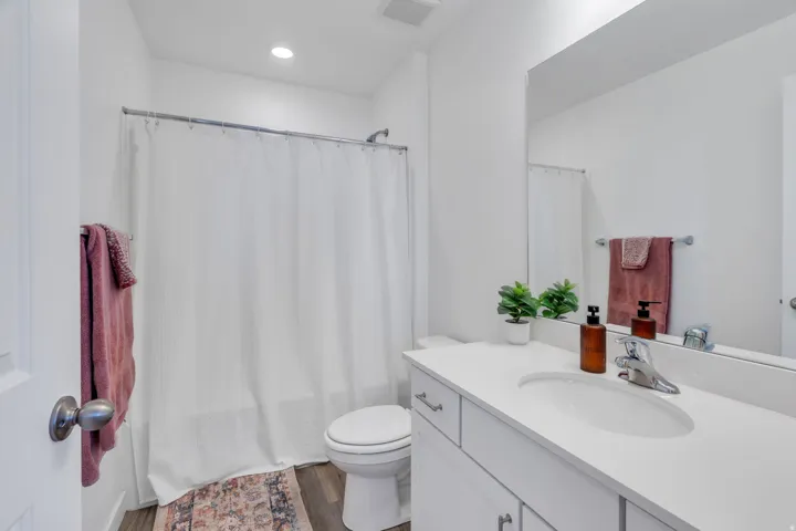 Recessed lighting, wood-finish flooring, white vanity with integrated sink, chrome faucet, and a large wall-mounted mirror