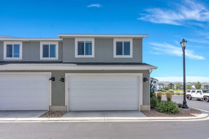 Two-story stucco exterior with white-framed windows, attached garages with white doors, and exterior wall sconces