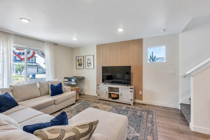 Recessed lighting throughout, wood-finish flooring, accent wall with vertical wood paneling, sliding glass door, and a built-in window