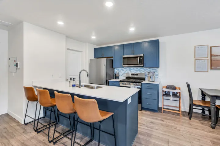 Kitchen island with white countertop, stainless steel appliances, blue cabinetry, wood-finish flooring, and recessed lighting