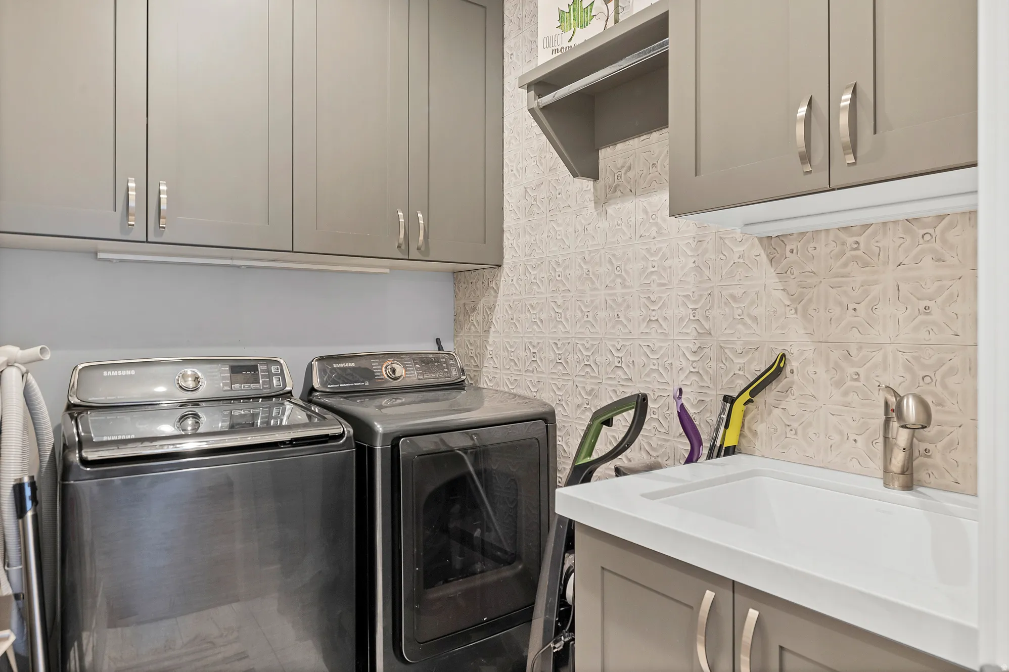 Light gray cabinetry with brushed nickel hardware, white countertop with integrated sink, and textured tile backsplash