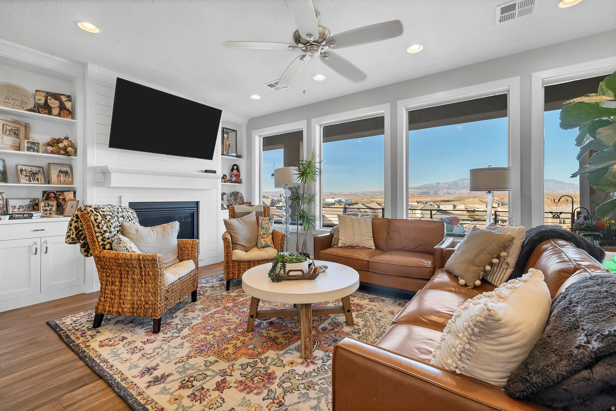Built-in shelving, a fireplace with a mantel, recessed lighting, wood-finish flooring, and expansive windows