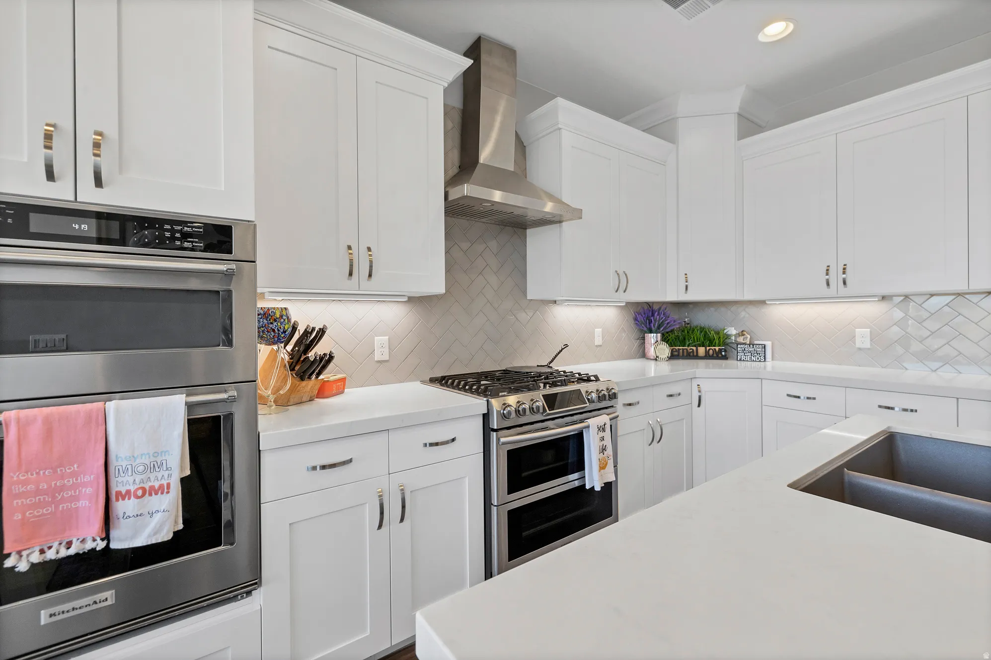 White shaker-style cabinetry, stainless steel appliances, quartz countertops, herringbone tile backsplash, and an undermount double basin sink