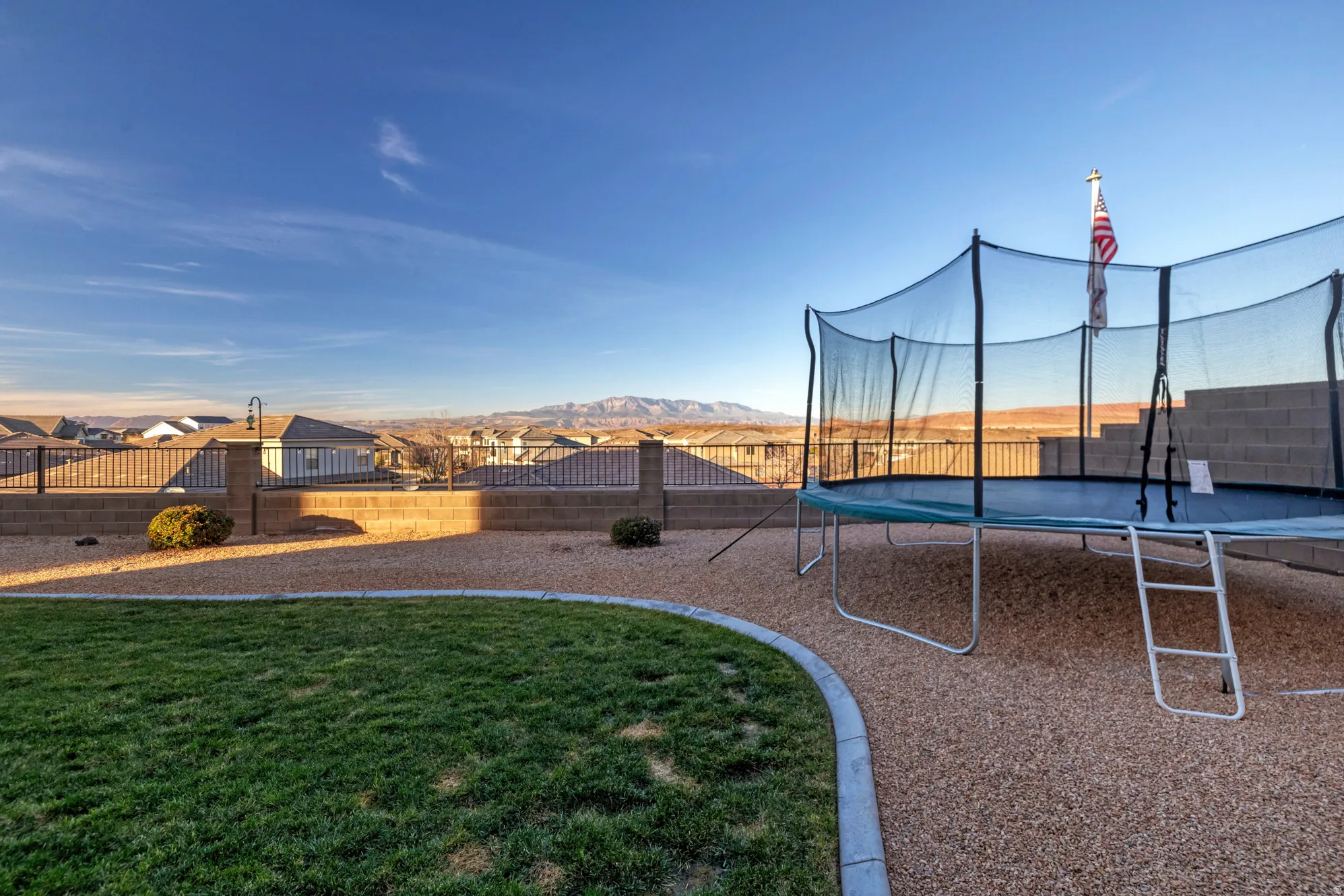 Expansive backyard featuring a manicured lawn, gravel landscaping, and a tiered block wall
